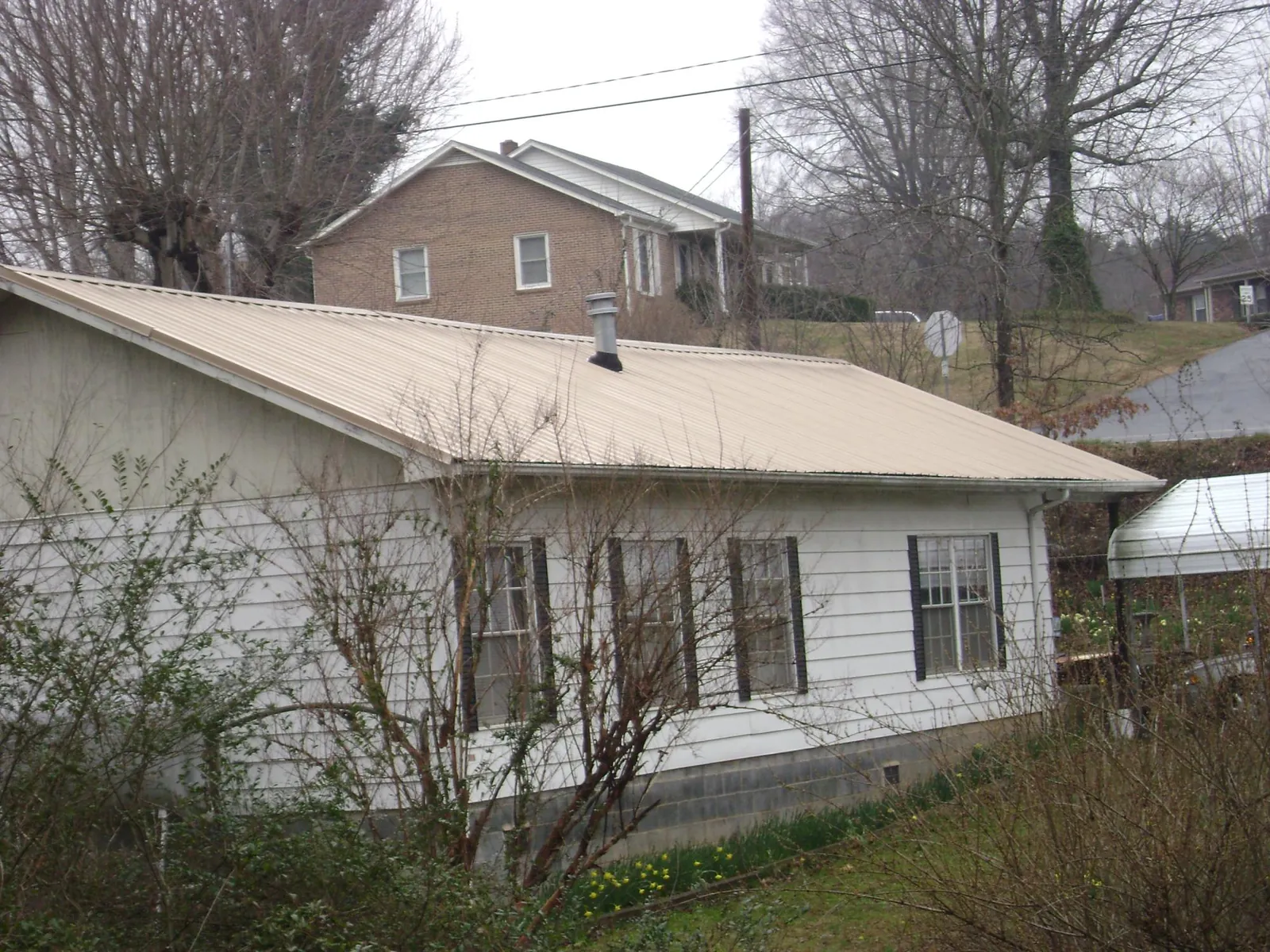 Tan metal roof on a white sided house set into a hillside — Commercial Roofing by Roofing Brothers in Odessa